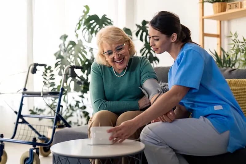 Caregiver checking the blood pressure of a smiling elderly woman at home