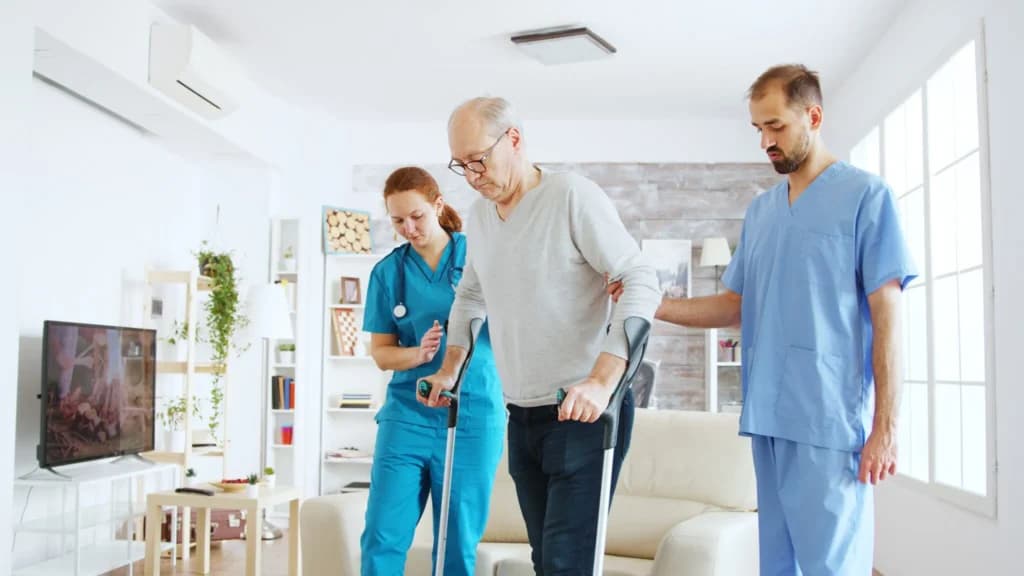 Team of nurses and social workers helping an older man walk with crutches